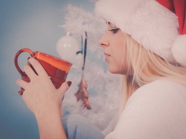 Noel zamanı konsepti sırasında rahatlama. Noel Baba şapkalı kadın elinde tatil kupası, sıcak içecek, kahve ya da çay içip dinlenmek için boş vaktinin tadını çıkarıyor..