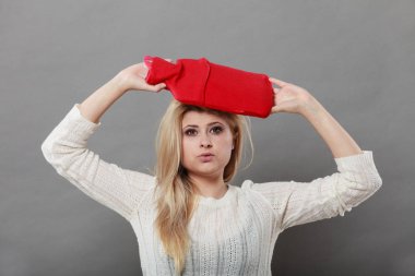 Baş ağrısı ile başa çıkmak için kırmızı sıcak su şişesi üzerinde kafa tutan kadın