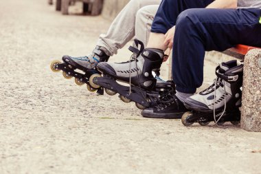 Closeup tekerlekli paten üzerinde açık koyarak insanların arkadaş. Kadın ve adam bankta oturan.