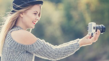Gülümseyen kadın giyen siyah şapka ve gri kazak dijital kamera açık fotoğraf oturum kullanarak fotoğraf çekmek. Tutku sahip erkek.