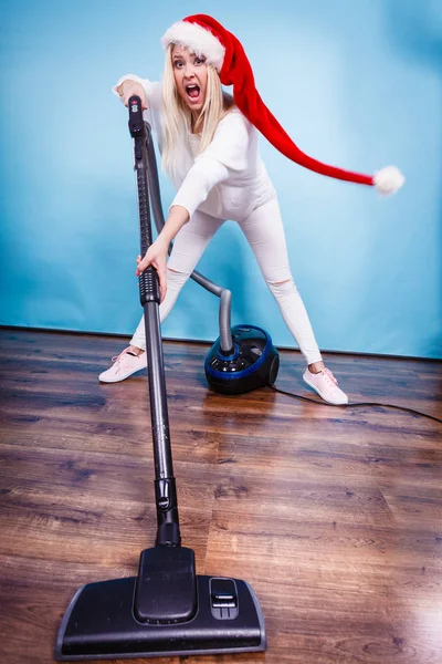 Woman vacuuming the house, last minute. Teen girl in santa helper hat with vacuum cleaner, angry furious face expression. Christmas time and housework concept.