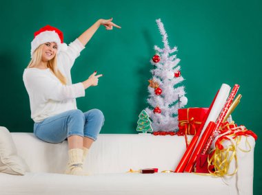 Dinlenme sırasında Noel kavramı. Noel Baba şapkası rahatlatıcı, mevsimlik ağaca işaret boş vaktinizi kanepede oturan sarışın genç kadın.