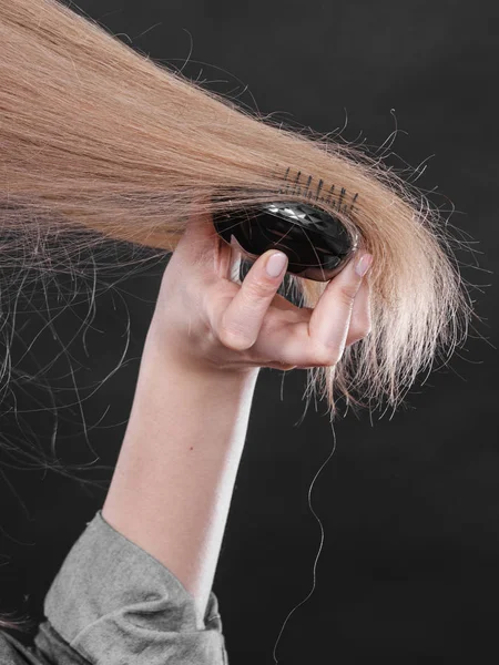 Everyday hygiene and care about good look. Back view of blonde casual girl combing her long straight hair. Woman using black comb hairbrush.