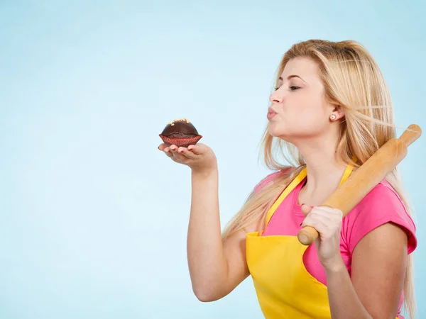 Baking tasty desserts sweets at home concept. Woman holding delicious chocolate cupcake and rolling pin wearing yellow apron.