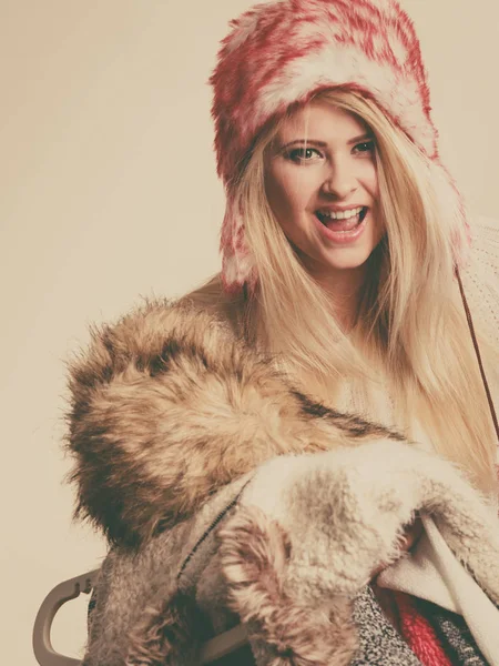 Accessories and clothing for cold days, fashion concept. Blonde woman in winter warm furry hat russian style holding big pile of clothes