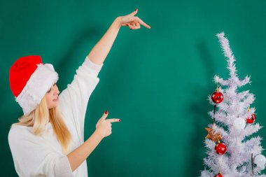 Sıcak bir tatil yeri, mevsimlik aksesuar konsepti. Noel Baba şapkalı sarışın genç kadın Noel ağacı süslüyor.