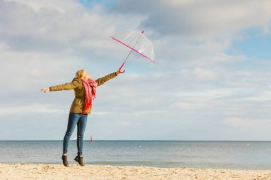 Mutluluk, büyük kavram duygu soğuk sonbahar havanın tadını. Deniz, güneşli ve açık mavi gökyüzü yakınındaki plajda şeffaf şemsiye ile atlama kadın