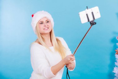 Modern tatil kavramı. Sarışın kadın kendini selfie smartphone sopa ile Noel resim çekmek Noel Baba şapkası.