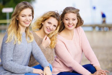 Üç modaya uygun kadın sıcak sonbahar havasında kazak giyip boş zamanlarını güneşli plajlarda geçiriyorlar. Moda modelleri dışarıda.