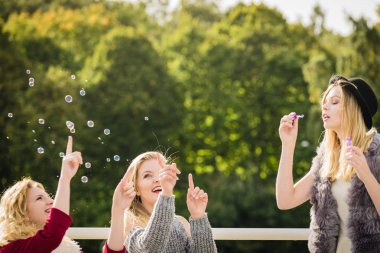 Tatil eğlencesi, arkadaşlık konsepti. Kadın arkadaşlar dışarıda sabun köpüğü üflerken eğleniyorlar..