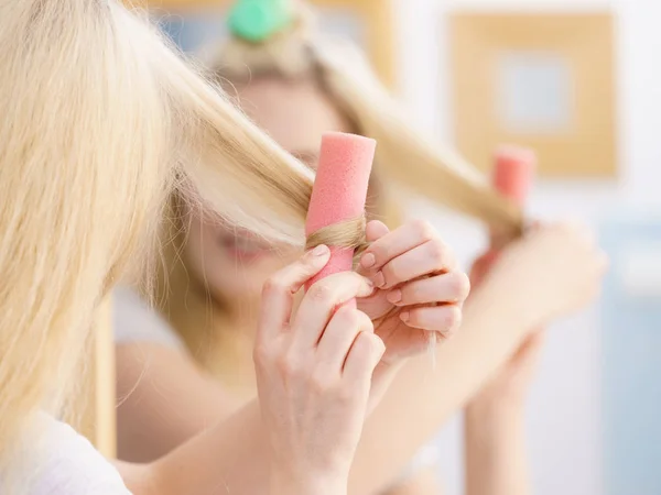 Blonde woman using hair rollers to create beautiful hairstyle on her hairdo.