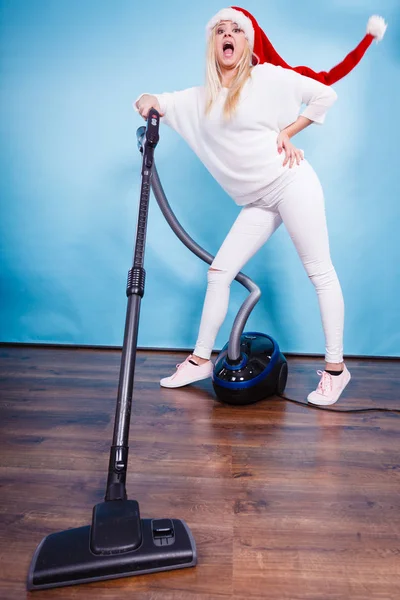 Woman vacuuming the house, last minute. Teen girl in santa helper hat with vacuum cleaner, funny face expression. Christmas time and housework concept.