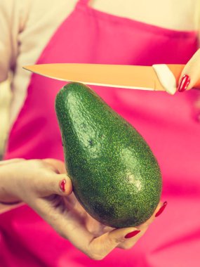 Kadın doğrama, yeşil sebze hazırlama, mutfak bıçağı kullanarak lezzetli avokado. Önlük giymiş bir kadın yemek yapıyor..