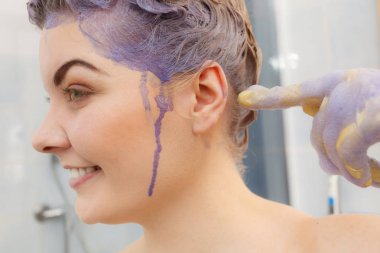 Kadın onun saç boyama şampuan uygulamak. Mor yıkama ürün olan erkek. Ev lekeli yanağını işaret tonlama sarı renk.