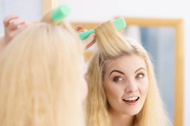 Saçında güzel bir saç stili yaratmak için saç maşası kullanan sarışın kadın..