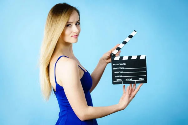 Woman holding professional film slate, movie clapper board. Hollywood production objects concept. Studio shot on blue background.