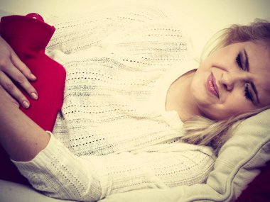 Ağrılı dönemler ve menstrüel kramp sorunları kavramı. Mide sahip kadın biraz rahatlama hissetmeye sıcak su şişesi tutan çok iyi duygu cofa yalan krampları