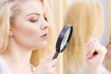 Bölünme sorunu, kuru etki, saç bakım konsepti. Mutsuz sarışın kadın büyüteçle zarar görmüş saçlara bakıyor.