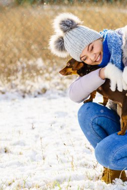 Genç kadın kış aylarında eğleniyor. Kar yağıyor küçük purebreed daksund köpek köpeği ile oynarken erkek