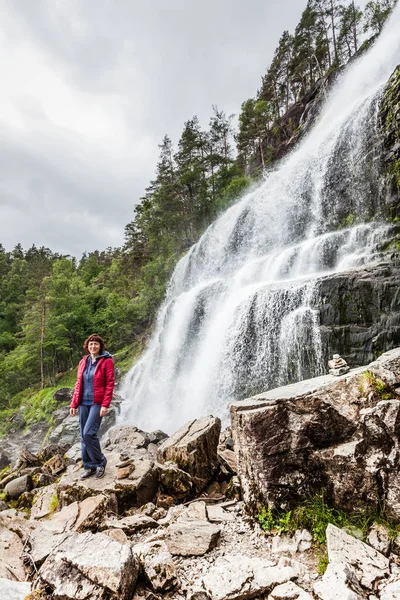 Tourist woman at Svandalsfossen in Norway, powerful waterfall in norwegian mountains. National tourist Ryfylke route.