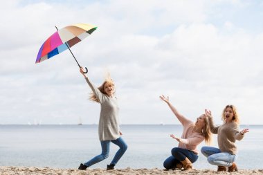 Üç kadın renkli şemsiyelerle hoplayıp zıplıyor. Bayan arkadaşlar dışarıda eğleniyor..