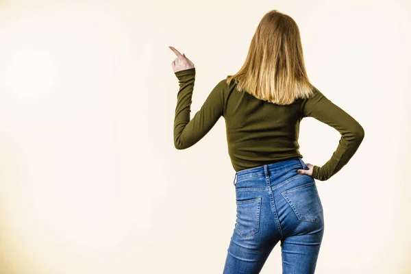 Back view of woman with blonde hair on white background showing something, pointing with finger at copy space.