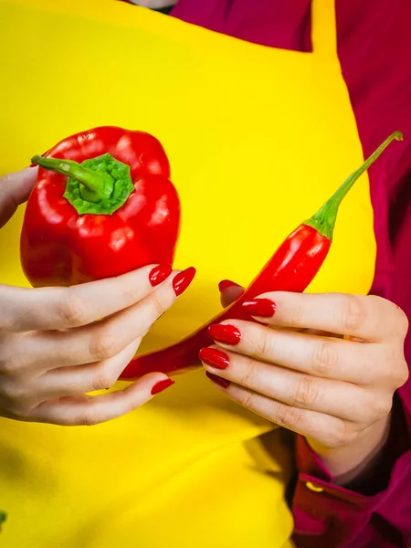 Woman comparing bell pepper and red hot chilli. Vegetables, spices, food concept.