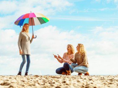 Birlikte harika vakit geçiren üç kadın. Renkli bir şemsiye tutan bir kadın.