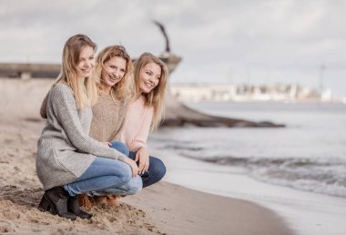 Üç modaya uygun kadın sıcak sonbahar havasında kazak giyip boş zamanlarını güneşli plajlarda geçiriyorlar. Moda modelleri dışarıda.