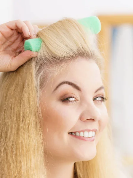 Blonde woman using hair rollers to create beautiful hairstyle on her hairdo.