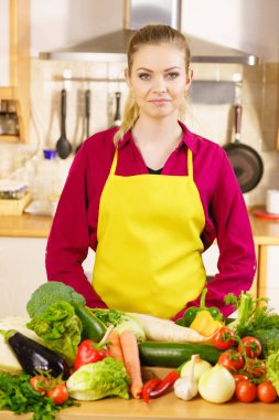 Mutfaktaki genç kadın sağlıklı ve vejetaryen bir şeyler pişirmek üzere olan bir sürü sebze yiyor.