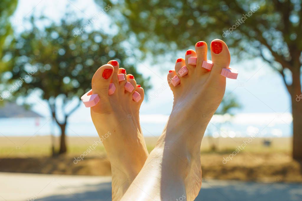 Woman waiting untill her feet nails dry on sun during summertime vacations. Female having toes separated.