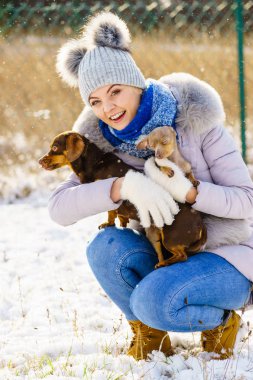 Genç bir kadın kışın eğleniyor. Kar yağarken iki küçük safkan köpek yavrusuyla oynayan dişi.