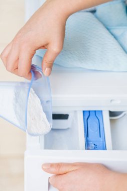 Çamaşır deterjanı ve ölçü kabının makineye dökülmesi. Ev işleri, çamaşır yıkama, obezite konsepti..