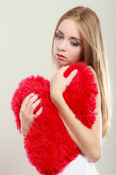 Broken heart love concept. Sad unhappy woman hugging red heart pillow closeup