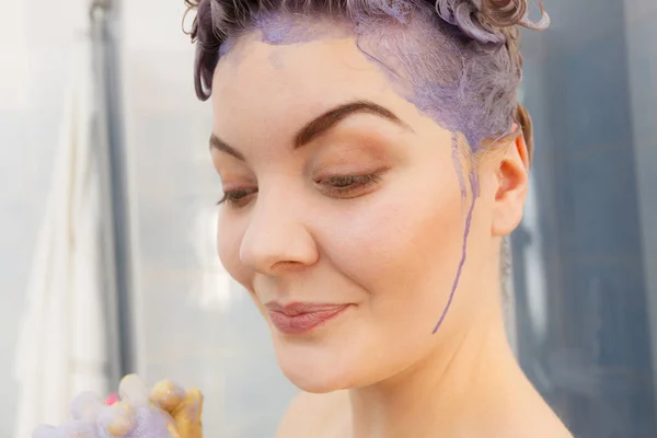 妇女应用着色洗发水在她的头发 女性有紫色洗涤产品 在家里打上金色的颜色 指着她被染红的脸颊 — 图库照片