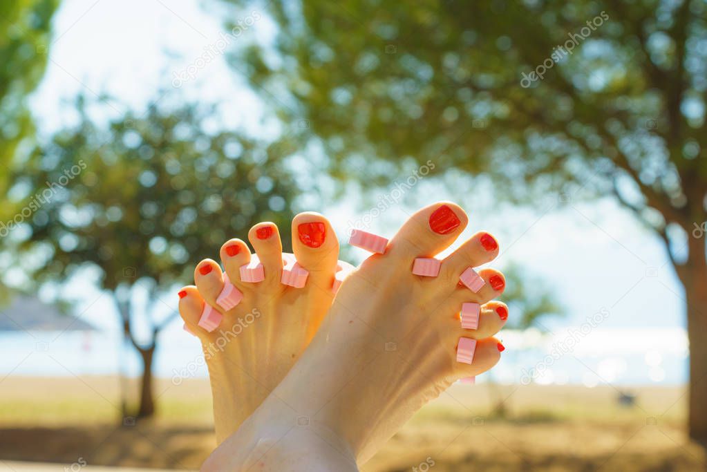 Woman waiting untill her feet nails dry on sun during summertime vacations. Female having toes separated.
