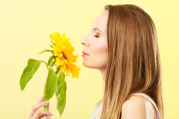Closeup portrait of attractive woman with sunflower in her hand on yellow background, side view