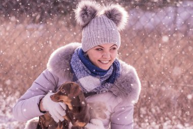 Genç bir kadın kışın eğleniyor. Kar yağarken iki küçük safkan köpek yavrusuyla oynayan dişi.