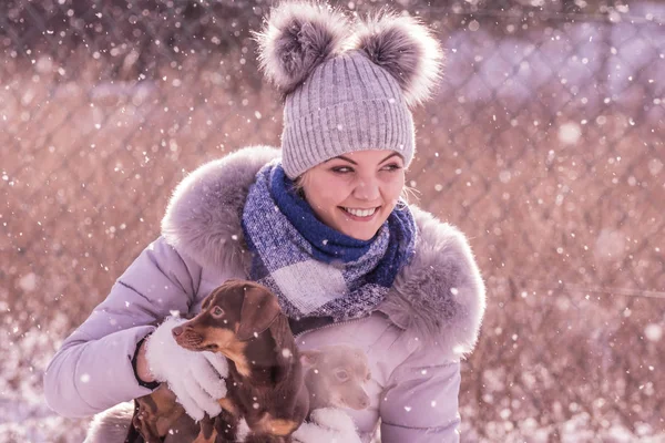 Genç bir kadın kışın eğleniyor. Kar yağarken iki küçük safkan köpek yavrusuyla oynayan dişi.