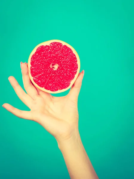 Healthy diet, refreshing food full of vitamins. Woman hand holding sweet delicious citrus fruit, red grapefruit.