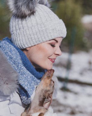 Genç bir kadın dışarıda karda eğleniyor. Dişi, soğuk kış gününde safkan köpek yavrusuyla oynuyor..