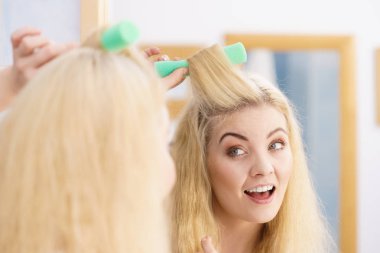 Saçında güzel bir saç stili yaratmak için saç maşası kullanan sarışın kadın..