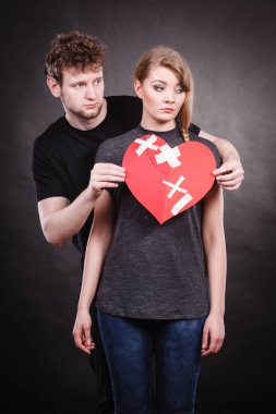 Kırık kalp zor aşk kavramı. Kadın üzgün mutsuz çift ve kağıt kırmızı kalp ile sabit tutan adam bandaj alçı. Yarığı ilişkiler.
