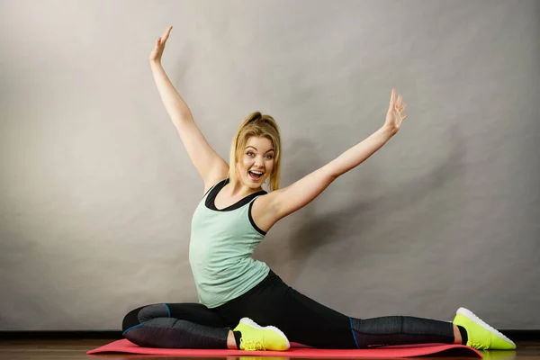 若いブロンドの女性スポーツウェア木製の床の屋内ストレッチ足に座っている 家でのトレーニング フィット感と健康 — ストック写真