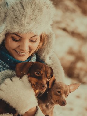 Genç bir kadın dışarıda karda eğleniyor. Dişi, soğuk kış gününde küçük safkan köpekleriyle oynuyor..