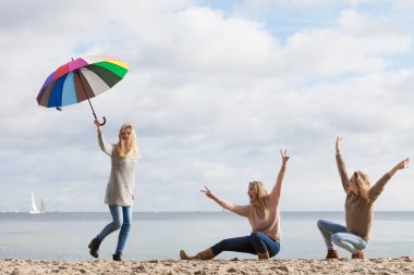 Üç kadın renkli şemsiyelerle hoplayıp zıplıyor. Bayan arkadaşlar dışarıda eğleniyor..