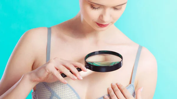 Skin control self examination concept. Yound woman holds magnifying glass in hand examining her body for melanoma suspicion. Checking benign moles.