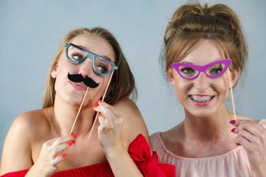 Sopanın üzerinde iki mutlu kadın gözlük takıyormuş gibi yaparak eğleniyorlar. Fotoğraf ve karnaval komik aksesuar konsepti.