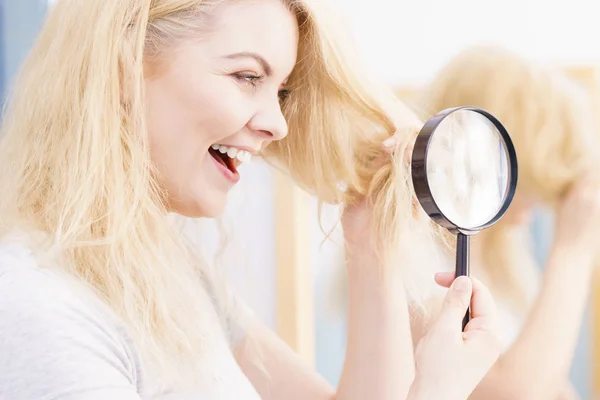 Happy woman magnifying her hair ends looking through magnifer being positive about conditioner results on her hairdor.